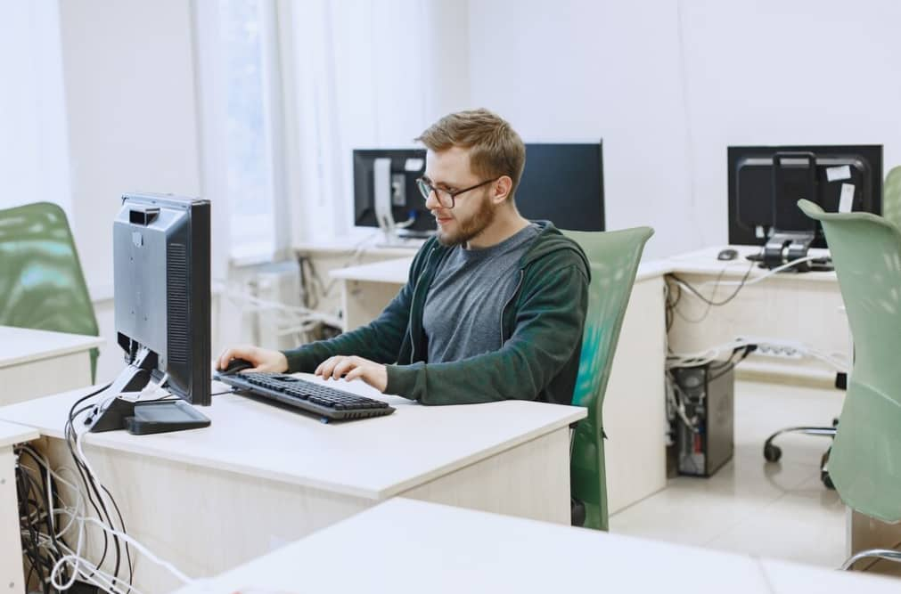 Man typing on a keyboard in a computer lab setting